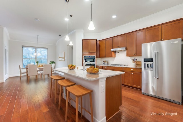 kitchen with a breakfast bar, decorative light fixtures, ornamental molding, appliances with stainless steel finishes, and an island with sink