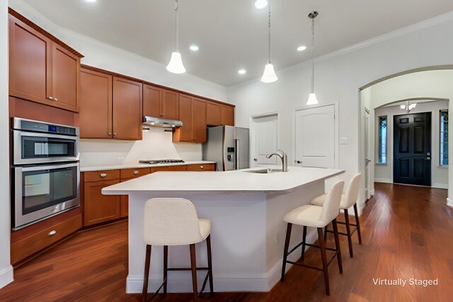 kitchen featuring dark wood-type flooring, sink, decorative light fixtures, a center island with sink, and stainless steel appliances