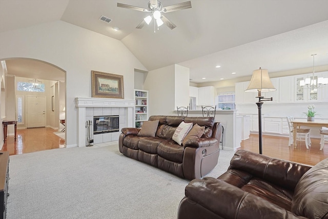 carpeted living room with a tiled fireplace, ceiling fan with notable chandelier, and high vaulted ceiling