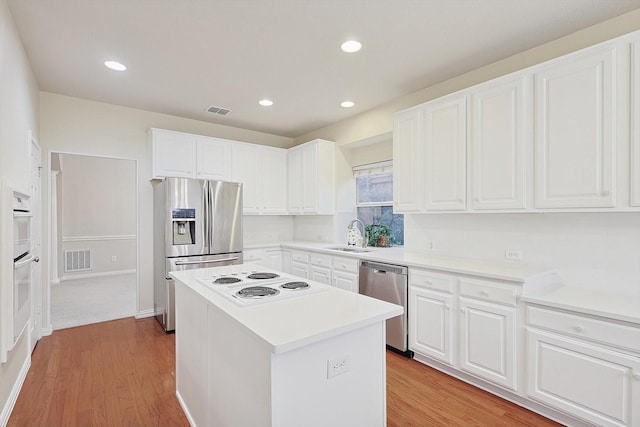 kitchen featuring stainless steel appliances, a center island, light hardwood / wood-style floors, and white cabinets