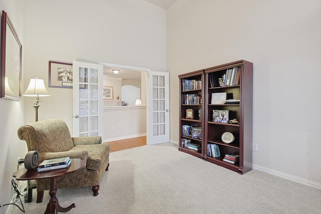 living area with light carpet, a towering ceiling, and french doors