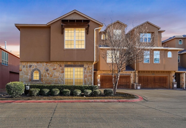 view of property featuring an attached garage, stone siding, driveway, and stucco siding