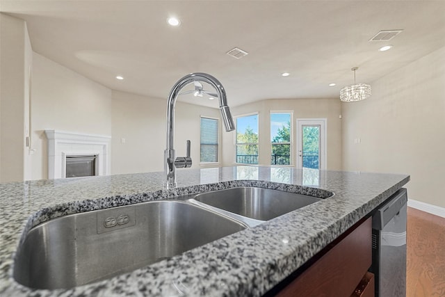 kitchen with hanging light fixtures, stone countertops, sink, and stainless steel dishwasher