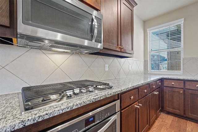 kitchen with light wood-type flooring, light stone countertops, stainless steel appliances, and decorative backsplash