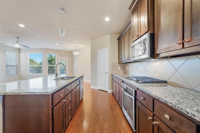 kitchen featuring a sink, hanging light fixtures, appliances with stainless steel finishes, light stone countertops, and an island with sink