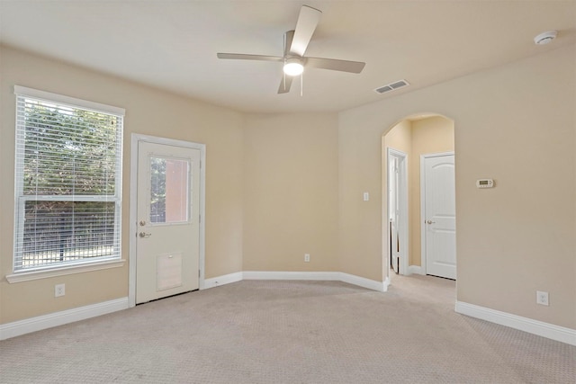 spare room with light carpet, baseboards, visible vents, arched walkways, and a ceiling fan