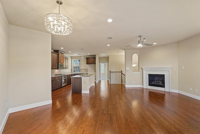 unfurnished living room featuring a tile fireplace, ceiling fan with notable chandelier, sink, and dark wood-type flooring