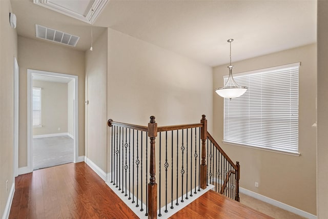 hallway with attic access, visible vents, baseboards, wood finished floors, and an upstairs landing