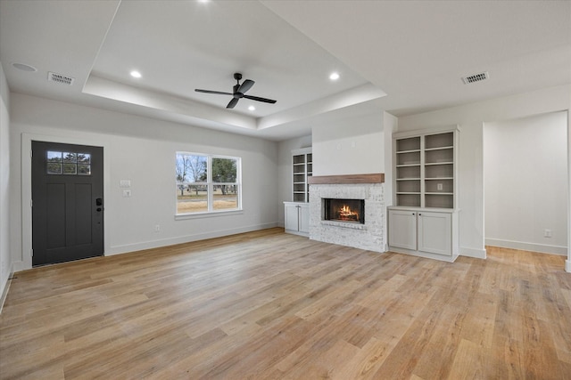 unfurnished living room featuring ceiling fan, a fireplace, light wood-type flooring, and a tray ceiling