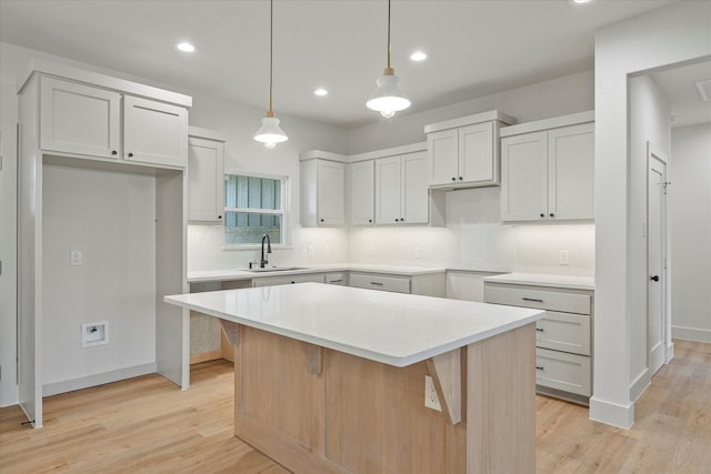 kitchen featuring decorative light fixtures, tasteful backsplash, sink, a center island, and light wood-type flooring