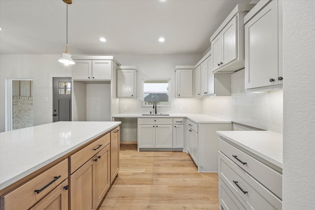 kitchen featuring hanging light fixtures, sink, white cabinets, and light wood-type flooring