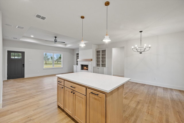 kitchen featuring a kitchen island, pendant lighting, a raised ceiling, light brown cabinets, and light hardwood / wood-style flooring