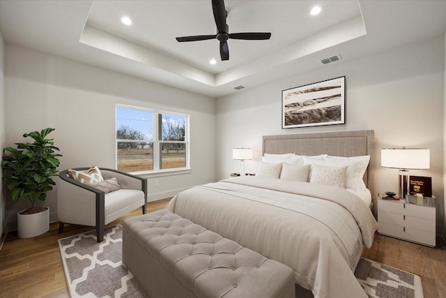 bedroom with ceiling fan, a tray ceiling, and light hardwood / wood-style flooring