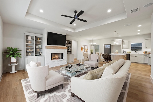 living room featuring sink, ceiling fan with notable chandelier, light hardwood / wood-style flooring, and a raised ceiling