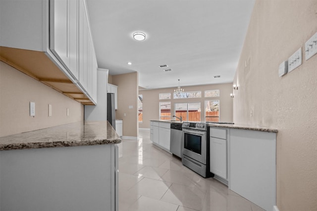 kitchen with an inviting chandelier, light stone countertops, a peninsula, white cabinets, and stainless steel appliances