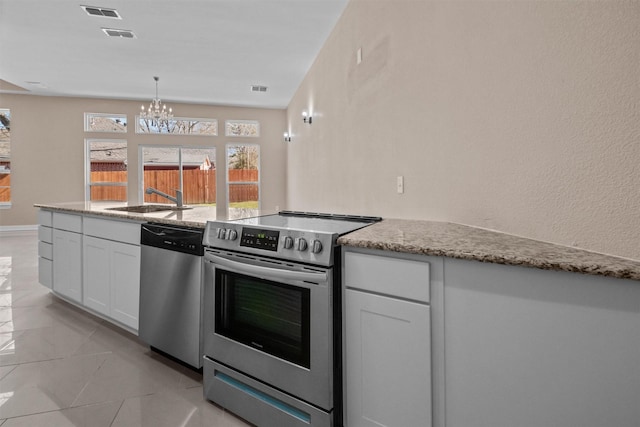 kitchen featuring a sink, an inviting chandelier, light stone counters, and appliances with stainless steel finishes