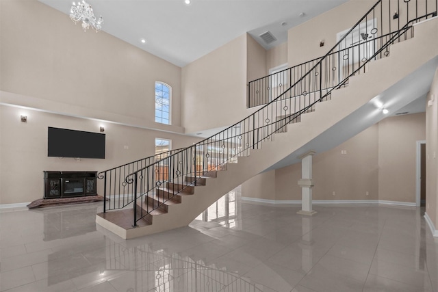stairs featuring a towering ceiling, a glass covered fireplace, visible vents, tile patterned flooring, and baseboards