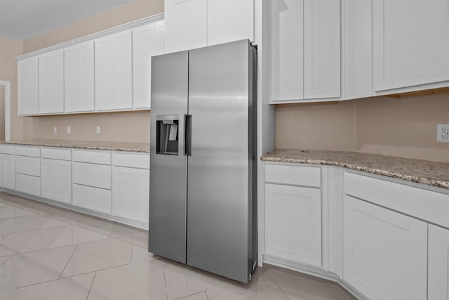 kitchen featuring light tile patterned flooring, stainless steel fridge with ice dispenser, light stone countertops, and white cabinets