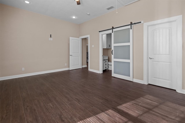 unfurnished bedroom featuring visible vents, baseboards, a barn door, and dark wood-style floors
