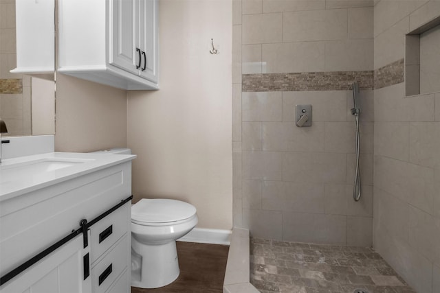 bathroom featuring baseboards, toilet, a tile shower, vanity, and wood finished floors