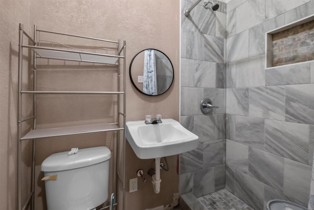 full bath with a textured wall, tiled shower, a sink, and toilet