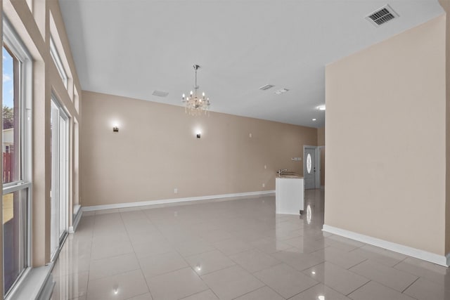 empty room featuring light tile patterned flooring, visible vents, baseboards, and an inviting chandelier