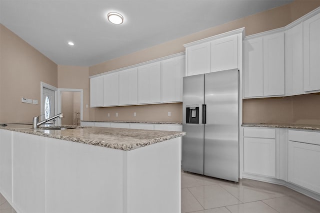 kitchen with white cabinets, stainless steel refrigerator with ice dispenser, light stone counters, a kitchen island with sink, and light tile patterned flooring