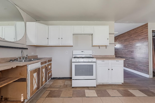 kitchen featuring wooden walls, white gas range oven, and white cabinets