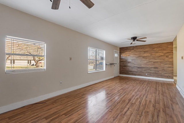 empty room featuring ceiling fan, wooden walls, and hardwood / wood-style floors