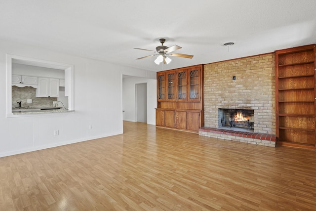 unfurnished living room featuring a textured ceiling, a fireplace, ceiling fan, and light wood-type flooring