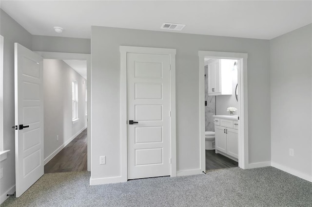 unfurnished bedroom with ensuite bath and dark colored carpet