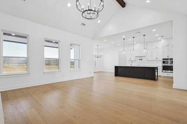 unfurnished living room featuring high vaulted ceiling, beamed ceiling, sink, a notable chandelier, and light wood-type flooring