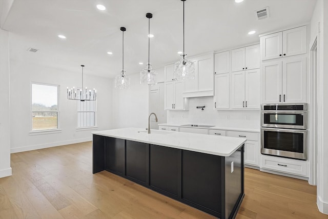 kitchen featuring white cabinetry, sink, hanging light fixtures, a kitchen island with sink, and stainless steel double oven