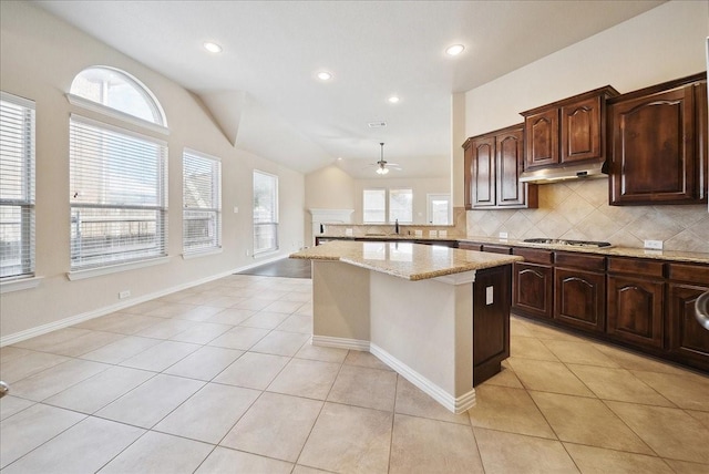 kitchen with light tile patterned floors, lofted ceiling, light stone countertops, and stainless steel gas stovetop