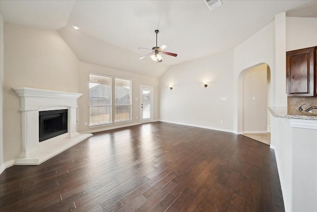 unfurnished living room featuring a fireplace with raised hearth, lofted ceiling, wood finished floors, visible vents, and a ceiling fan