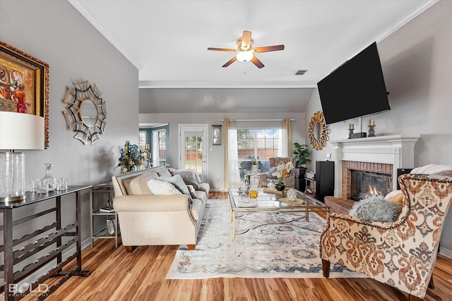 living room with ornamental molding, a fireplace, vaulted ceiling, and light wood-type flooring