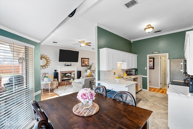 dining area featuring ceiling fan, ornamental molding, sink, and a brick fireplace