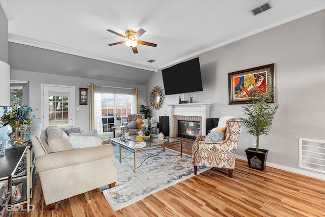 living room featuring lofted ceiling, ceiling fan, a fireplace, ornamental molding, and light wood-type flooring