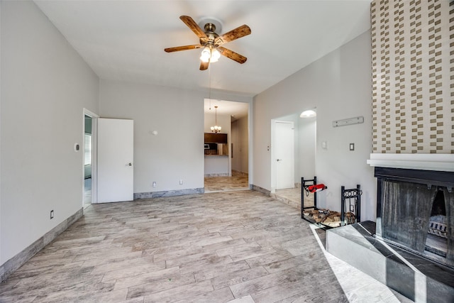 unfurnished living room featuring ceiling fan with notable chandelier and light wood-type flooring