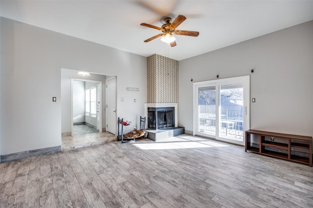 unfurnished living room with a tile fireplace, ceiling fan, and light wood-type flooring