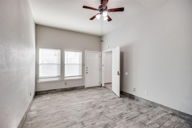 spare room with ceiling fan, a towering ceiling, and light wood-type flooring