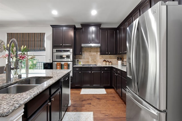 kitchen with sink, dark wood-type flooring, appliances with stainless steel finishes, dark brown cabinetry, and light stone countertops