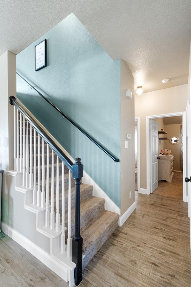 stairway with wood-type flooring and a textured ceiling