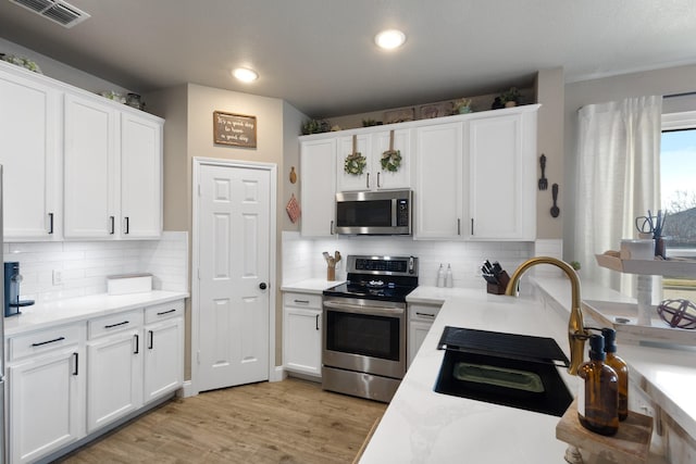 kitchen featuring stainless steel appliances, backsplash, white cabinets, and light hardwood / wood-style floors