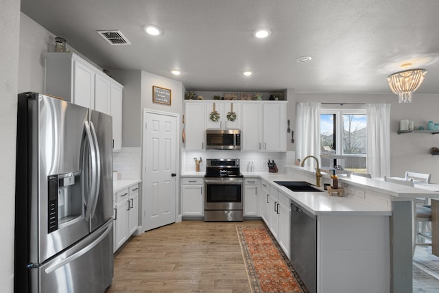 kitchen featuring appliances with stainless steel finishes, sink, white cabinets, a kitchen bar, and light hardwood / wood-style flooring