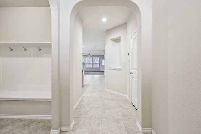 hall with arched walkways, light tile patterned flooring, and baseboards