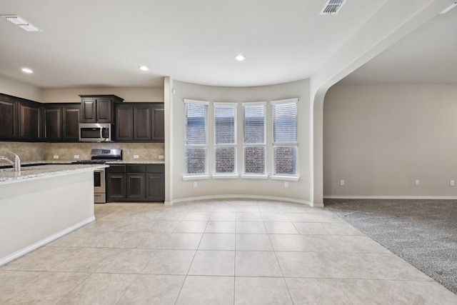 kitchen with arched walkways, visible vents, decorative backsplash, appliances with stainless steel finishes, and light carpet