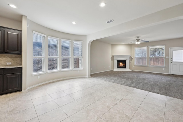 unfurnished living room with light tile patterned floors, visible vents, light colored carpet, a lit fireplace, and recessed lighting