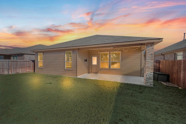 back of property at dusk with a patio area, a fenced backyard, and a lawn