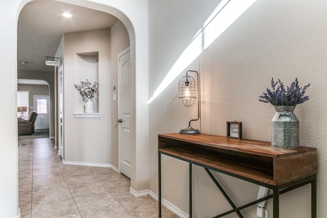 corridor featuring light tile patterned floors, baseboards, and arched walkways